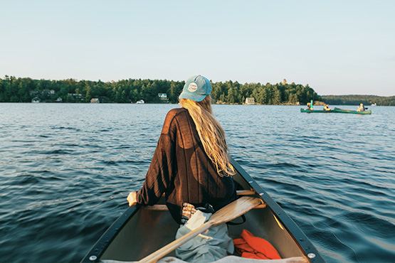girl with backwards hate in front of canoe on lake
