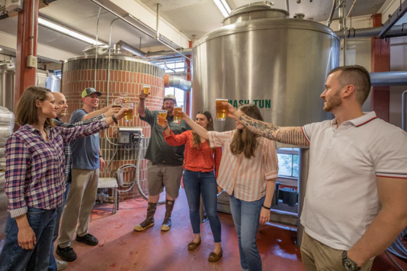 group of people holding up drinks inside a brewery