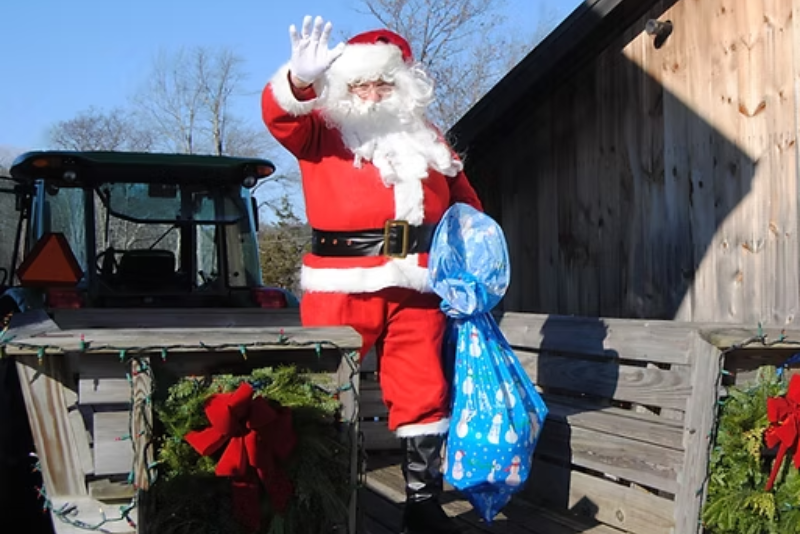 Santa Claus in red suit waving from back of a truck on a farm
