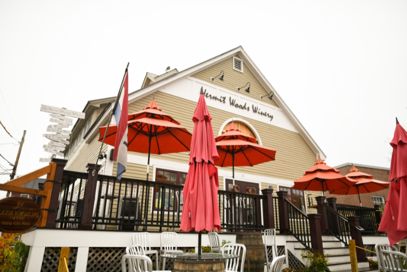 exterior of hermit woods winery in nh with red umbrellas and patio seating