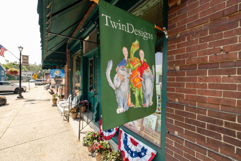green flag reads "Twin Designs" outside of brick storefront