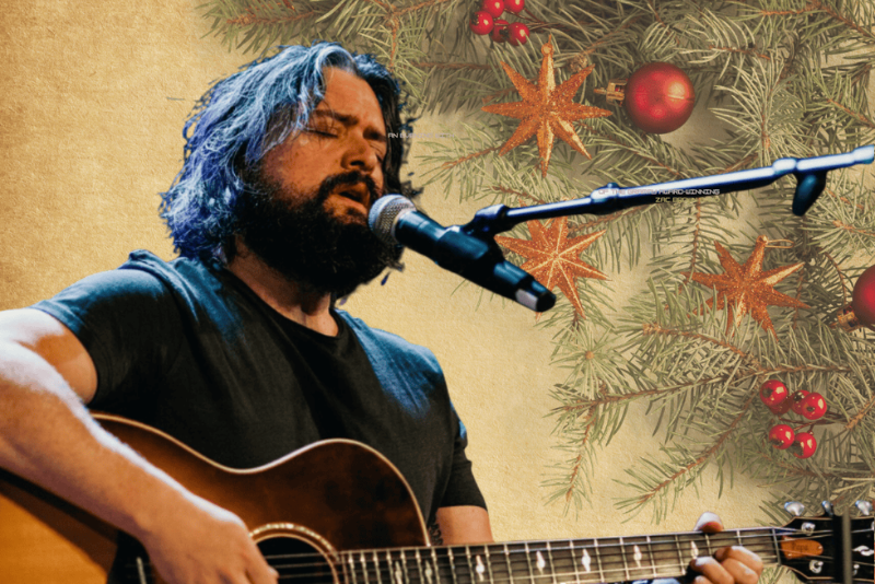 singer at microphone stand playing guitar against a christmas-inspired graphic backdrop
