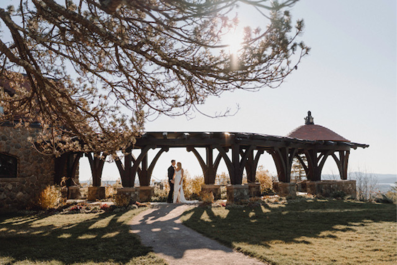 far-away shot of bride and groom under wooden structure at castle in the clouds